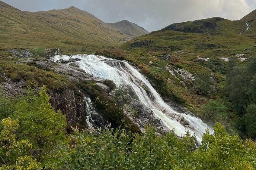 Ett vattenfall som störtar nerför en bergssluttning, omgivet av frodig grönska. 4