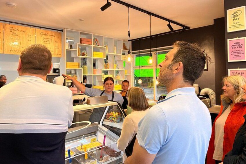 A food stall with a menu board, a person pointing at the menu, and a counter with food items. 2