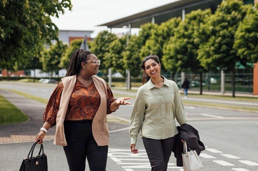 Two women walking on a crosswalk, one carrying a handbag and the other holding a jacket. 2
