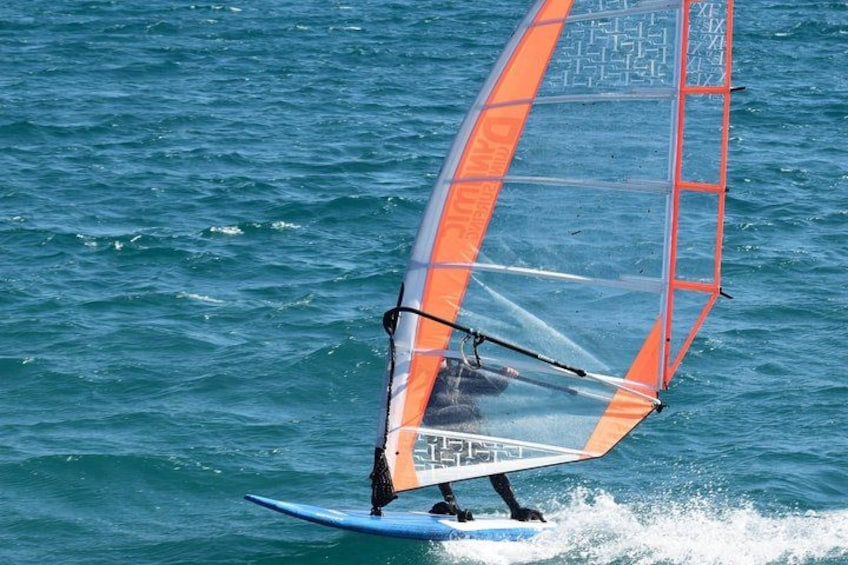 A person windsurfing on a blue board with an orange sail. 2