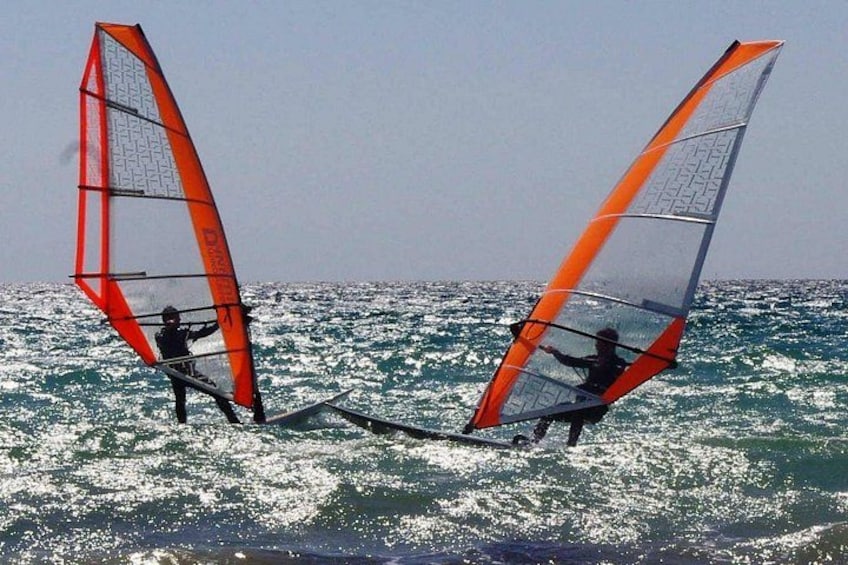 Two people windsurfing with orange sails on a body of water. 1