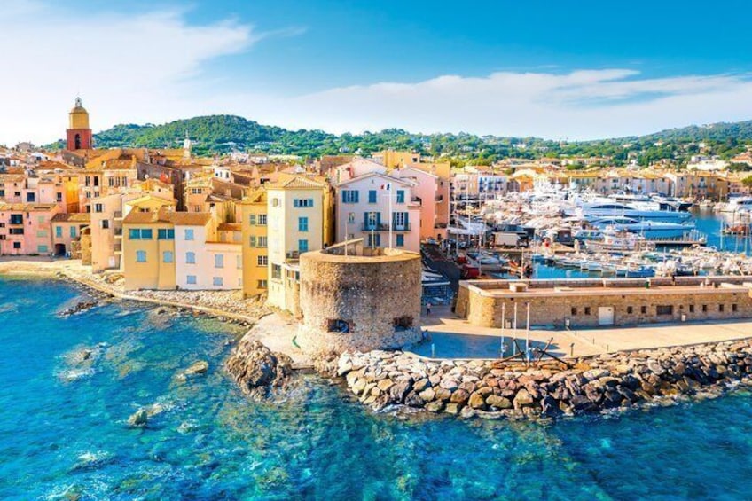 A coastal town with colorful buildings, a historic tower, and a marina with boats. 5