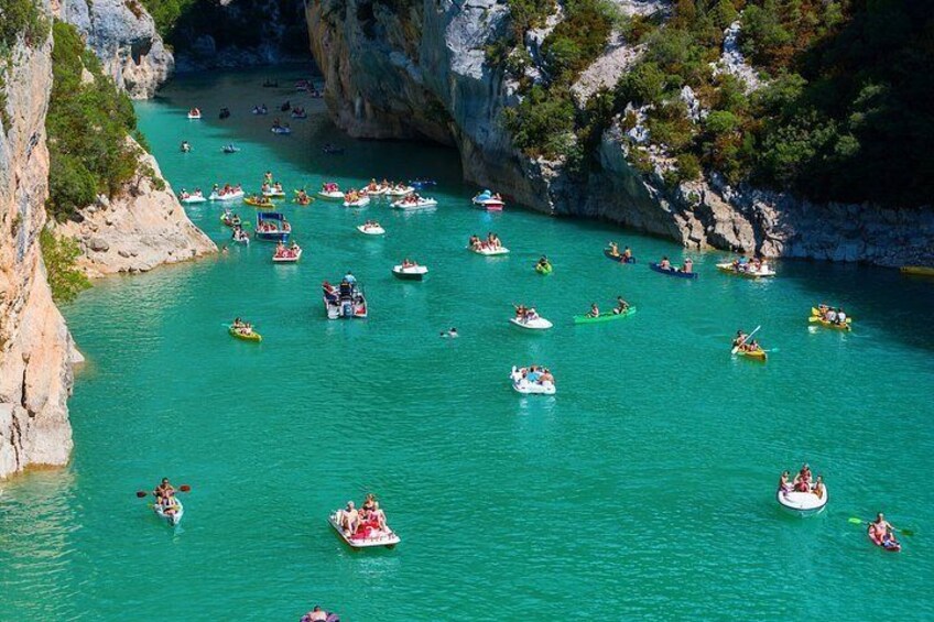 A turquoise river with numerous boats, surrounded by rocky cliffs and sparse vegetation. 4