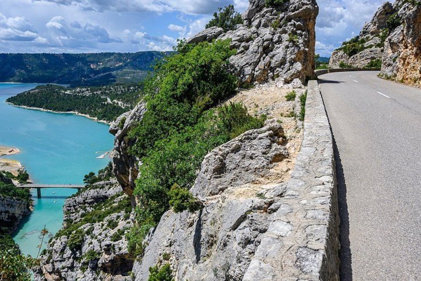 A winding road along a rocky cliffside with a view of a turquoise sea and a bridge. 4