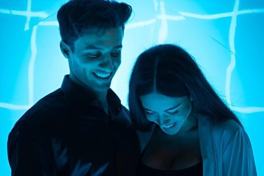 Two people standing in front of a blue-lit background with geometric patterns. 1
