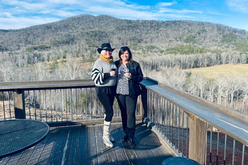 Two people on a wooden deck with a mountainous landscape in the background. 4