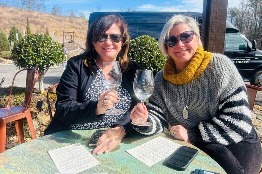 Two people sitting at a table with a menu, holding wine glasses, and a parked car in the background. 3
