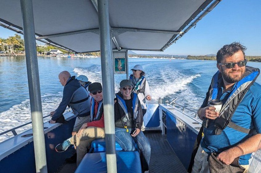 A group of people on a boat, wearing life jackets, with a calm body of water and a clear sky in the background. 5