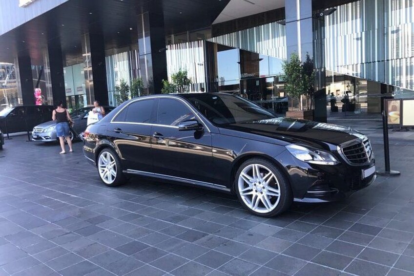 A black luxury car parked in front of a modern building with reflective glass windows. 2