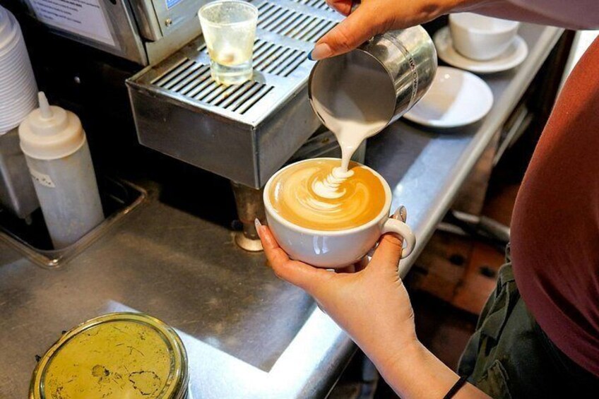 Une personne verse du lait dans une tasse de café, avec une machine à café et une tasse d’expresso en arrière-plan. 4