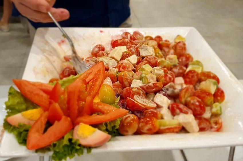 A white rectangular plate with a salad consisting of tomatoes, cucumbers, olives, and other vegetables. 4
