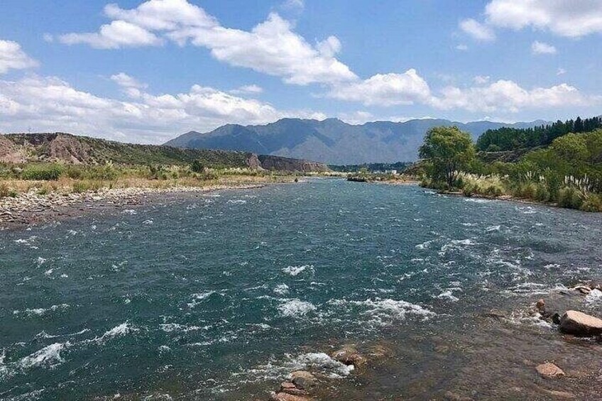 Un río con aguas cristalinas, rodeado de colinas y montañas bajo un cielo azul. 4