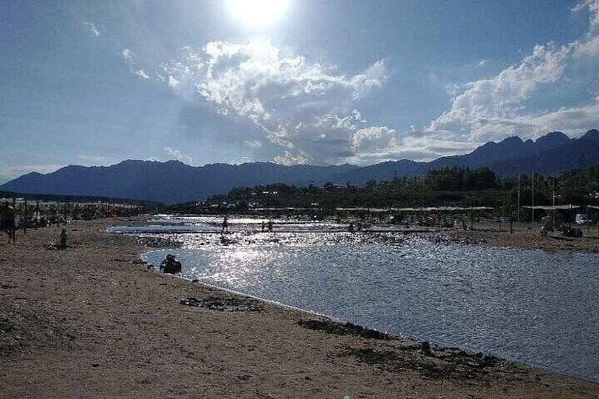 Orilla de río con montañas al fondo, una playa de arena y cielo despejado. 3