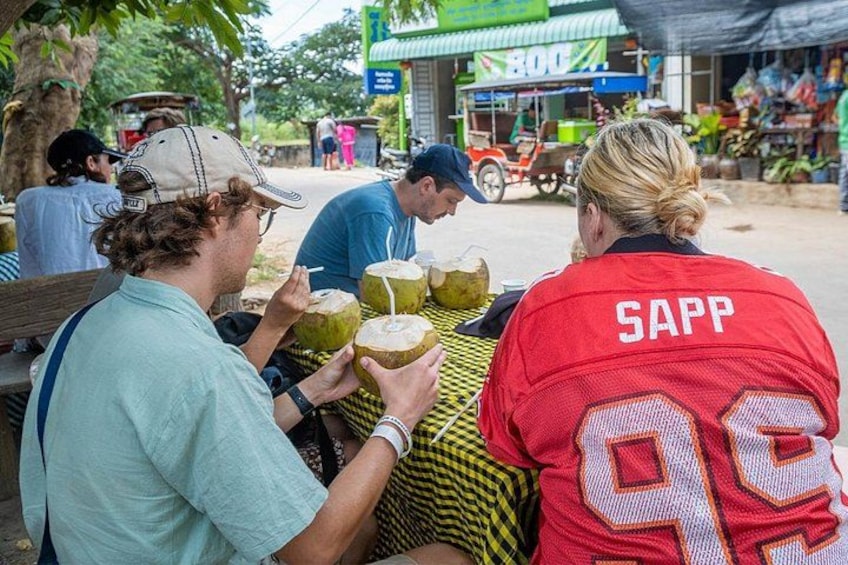 Mensen zitten aan een tafel, een persoon draagt een rode jas met 'SAPP' op de rug, en een tuk-tuk is op de achtergrond te zien. 5