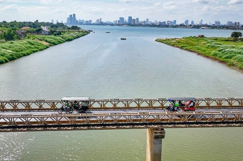 A river with a bridge, a city skyline in the background, and a few boats on the water. 1