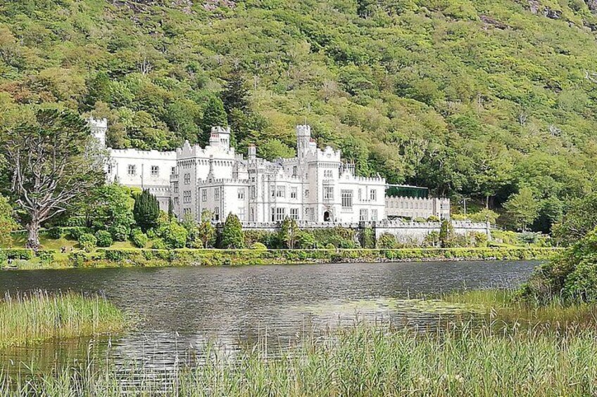 A large white castle with turrets, surrounded by lush greenery and a calm lake. 1