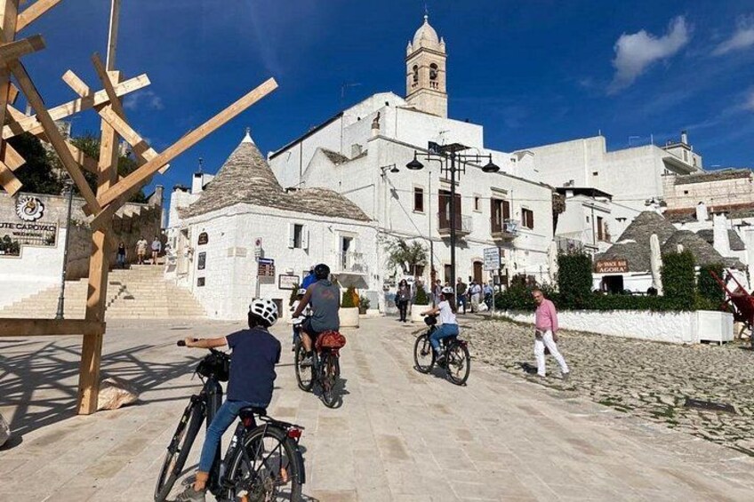Une scène de rue avec des bâtiments blancs, une tour et des personnes à vélo. 5
