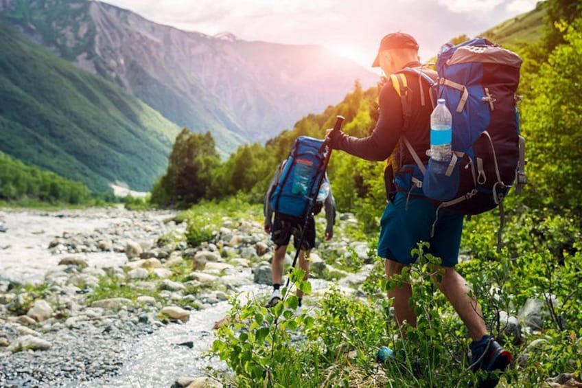 Two hikers with backpacks on a rocky trail surrounded by greenery and mountains. 2
