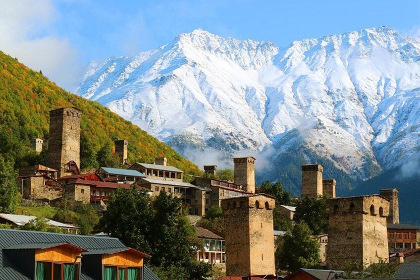 A historic town with medieval architecture, including towers and a church, nestled against a backdrop of snow-capped mountains. 1