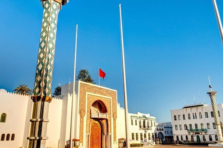 A traditional gate with a red flag, a tall minaret, and white buildings with arches. 1
