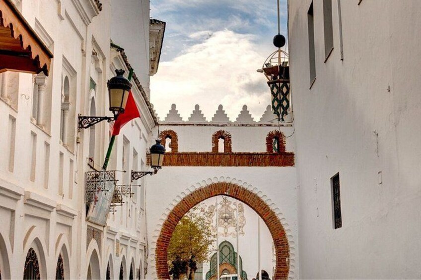 A white building with a red flag, a large arched gateway, and a decorative brick archway. 2