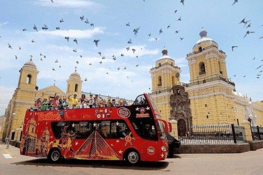 Un autobus à deux étages rouge, rempli de passagers, est garé devant un bâtiment historique doté de deux tours. 1