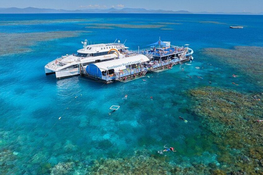 A large boat docked at a coral reef with clear blue water and a few people swimming. 1