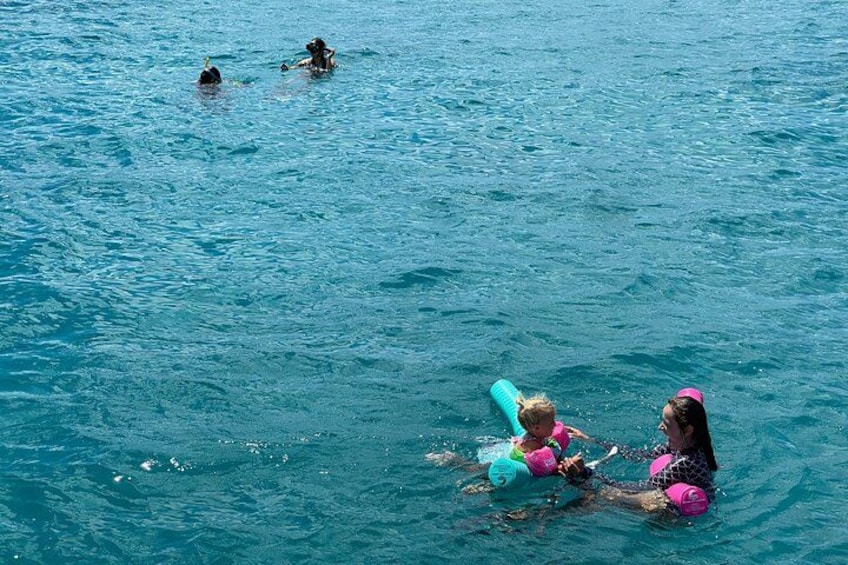 Two people floating on water with a child, and another person swimming in the background. 1