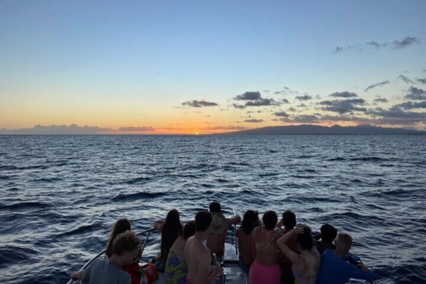 Un grupo de personas en un barco al atardecer, con el océano y una costa lejana al fondo. 2