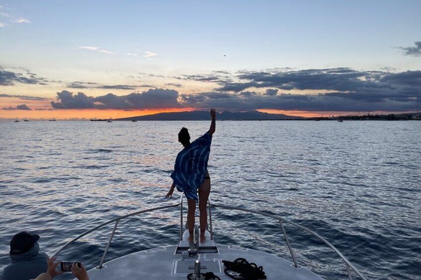 A person standing on a boat's deck, facing the water during sunset. 4