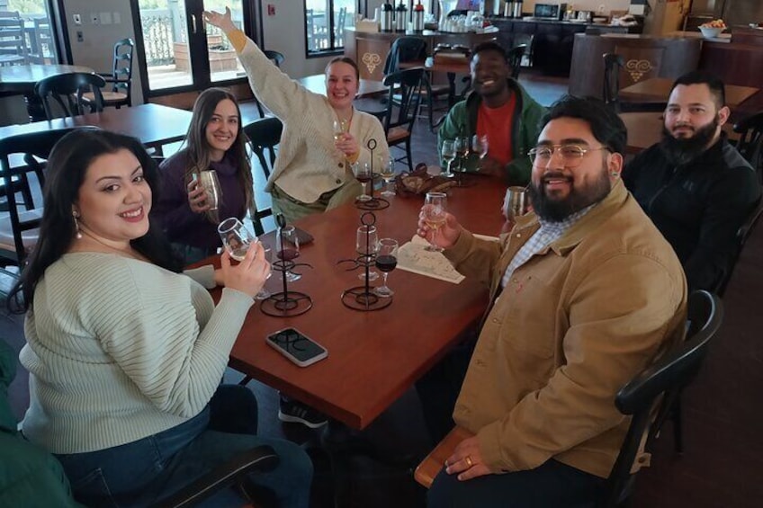 A group of people sitting around a table with wine glasses and bottles. 4