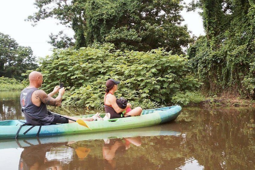 Two people in a green kayak on a calm river, surrounded by lush greenery. 5