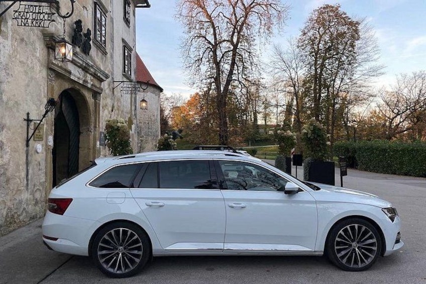 En vit kombibil parkerad framför en byggnad med en skylt där det står ”HOTEL GRAND OUEST”. 3