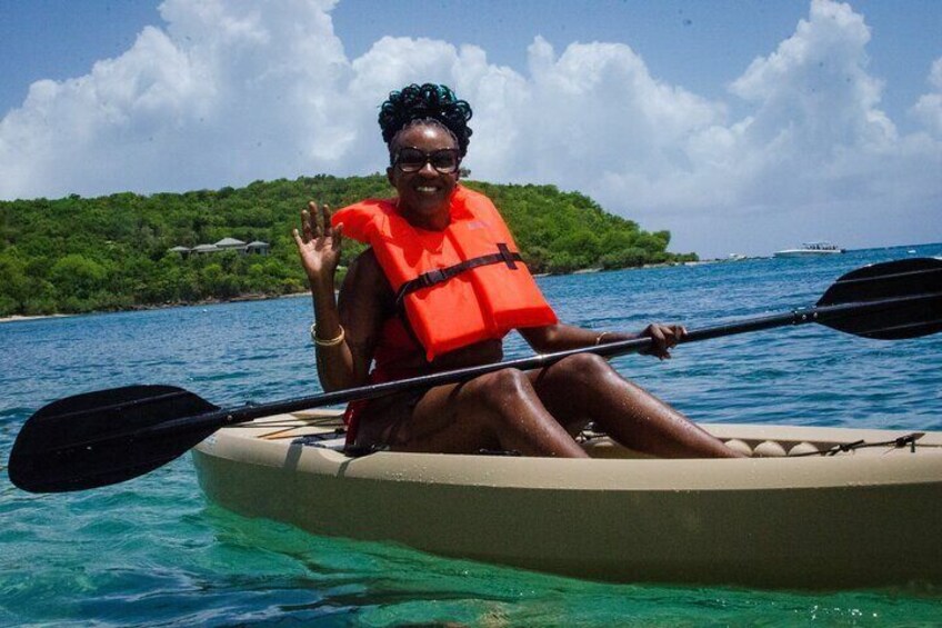 A person in a kayak on a body of water with a green island in the background. 1