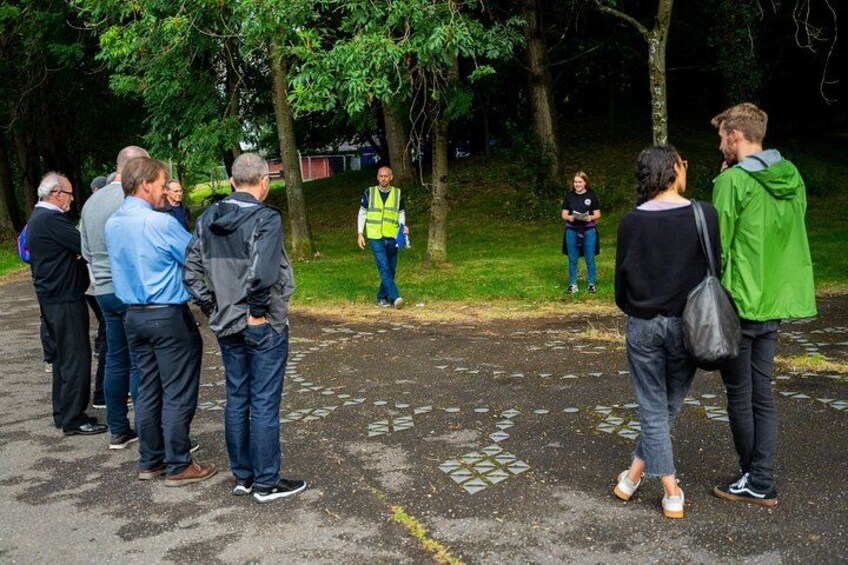 A group of people standing on a paved path in a park, surrounded by trees. 2