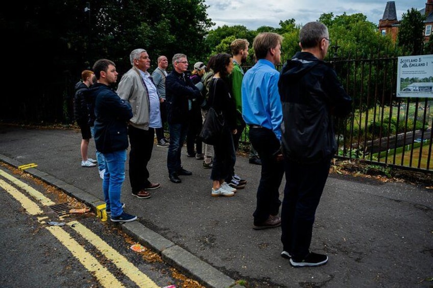 A group of people standing on a paved path, a fence, and a signboard. 3
