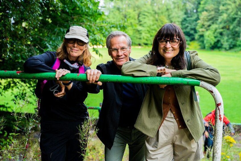 Three people leaning on a green metal structure in a park with greenery in the background. 4
