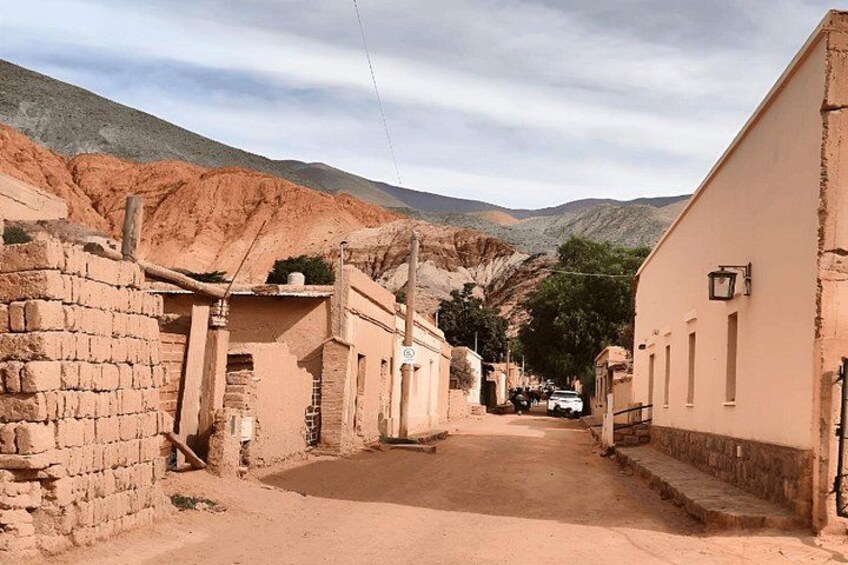 A narrow street in a desert town with adobe buildings, a white car, and mountains in the background. 5