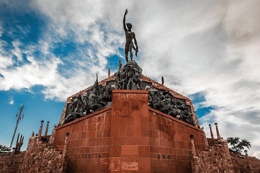 Un grand monument de pierre, orné d’une statue centrale, entourée de statues et de reliefs plus petits, se dressant sur un ciel partiellement nuageux. 2
