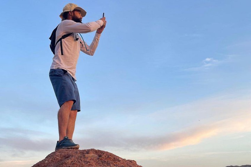 Una persona de pie sobre una roca con una mochila, fotografiando el cielo. 1