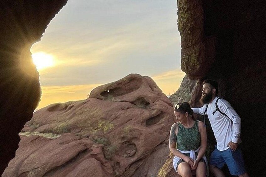 Two people sitting on a rock formation with a sunset in the background. 1