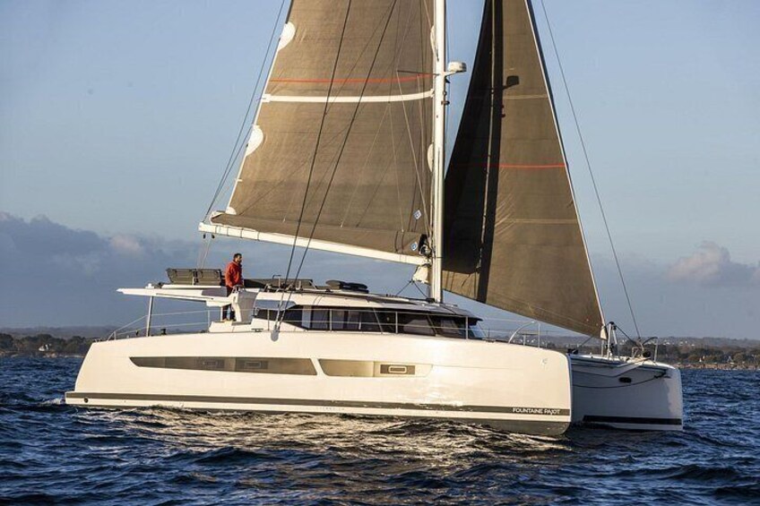 En vit yacht med en person som står på däck och seglar på vattnet. 5