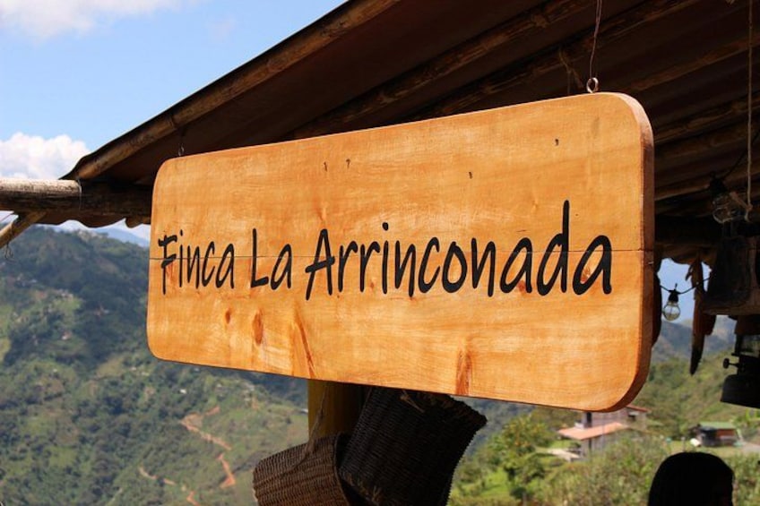 A wooden sign with the text 'Finca La Arrinconada' against a mountainous backdrop. 2