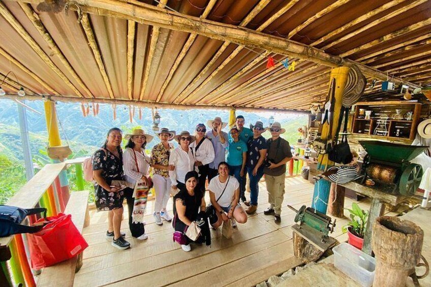 A group of people on a wooden deck with a bamboo roof, surrounded by various items and a scenic view. 3