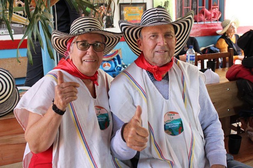 Two people wearing traditional attire with a sombrero, a white shirt, and a red scarf. They are giving a thumbs-up gesture. 3