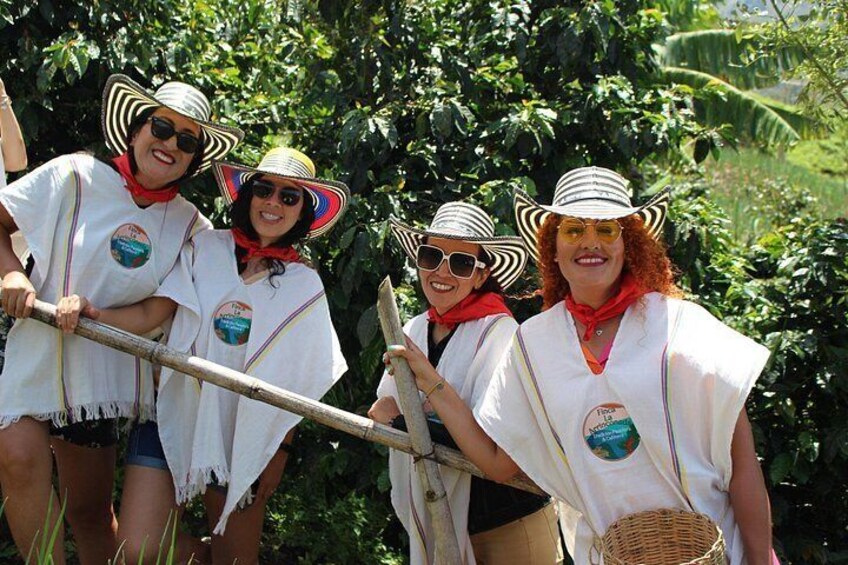 Four people in white ponchos with straw hats, holding a wooden structure, standing in a lush green environment. 3