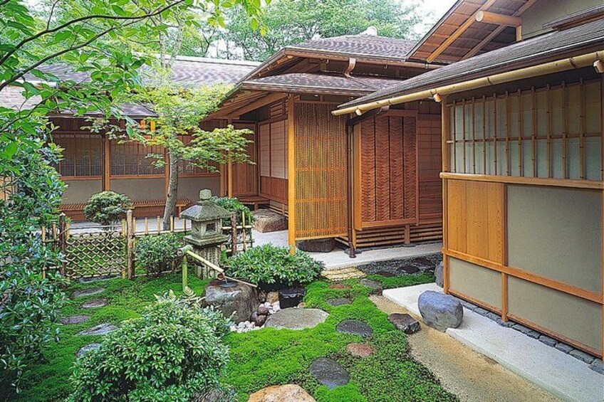 A traditional Japanese garden with wooden buildings, moss, rocks, and a stone lantern. 4