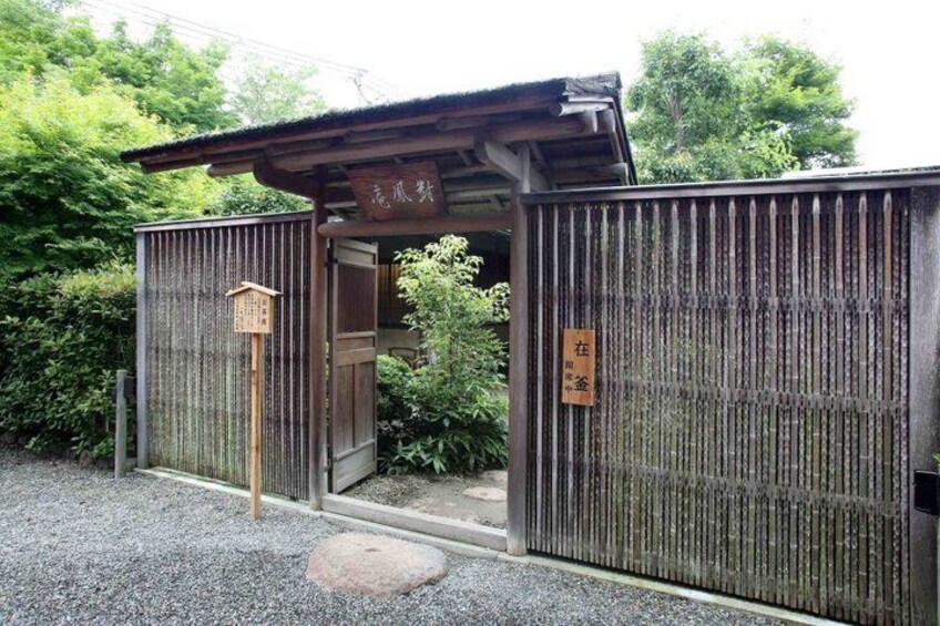 A traditional Japanese gate with a wooden signboard, surrounded by gravel and greenery. 3