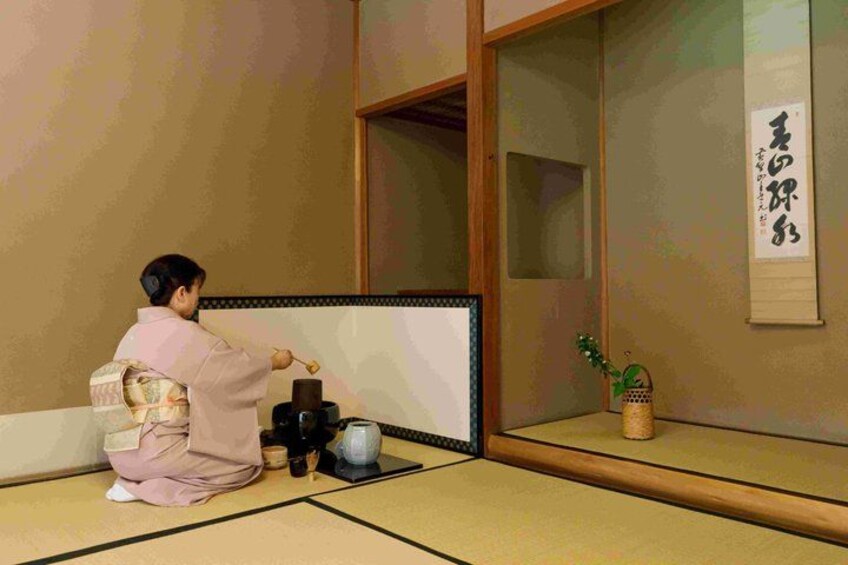 A person in traditional attire sitting on tatami mat floor, facing a shoji screen with calligraphy. 2