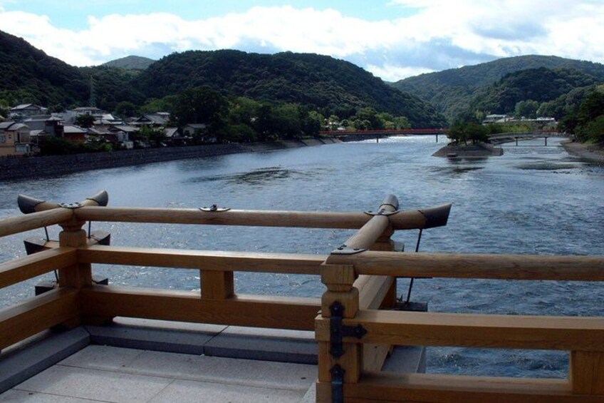 A wooden bridge over a river with houses and hills in the background. 5